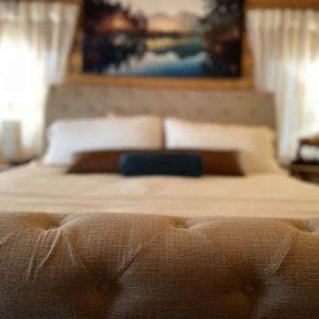 A large king-sized bed with a duvet is positioned at the center of the room, flanked by matching nightstands with stylish lamps that emit a soft, warm glow.