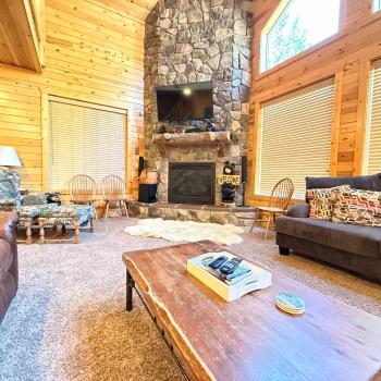 Relax in the grand living room, featuring a magnificent floor-to-ceiling stone fireplace, comfortable plush sofas, and a rustic live-edge coffee table.