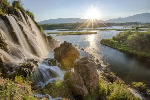 A waterfall spilling over boulders into a river at sunrise