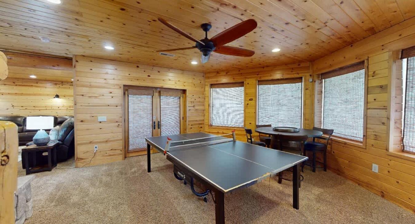 The basement of the cabin has been transformed into a vibrant and cozy game room, offering a perfect retreat for fun and relaxation. Near the far wall, there is a small seating area with a few comfortable chairs and a table.