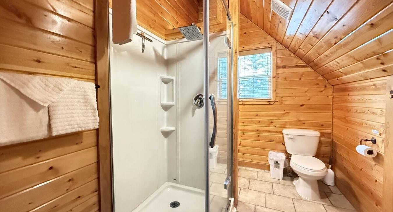 Bathroom upstairs with a standing shower, toilet, sink, and shelves for storage.