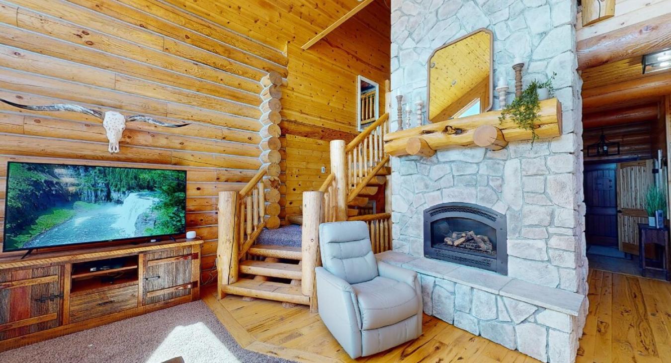 Imagine walking into a cozy yet spacious living room in a cabin, where rustic charm meets comfort. The focal point of the room is a grand stone fireplace, its warm hearth crackling with a soft fire.