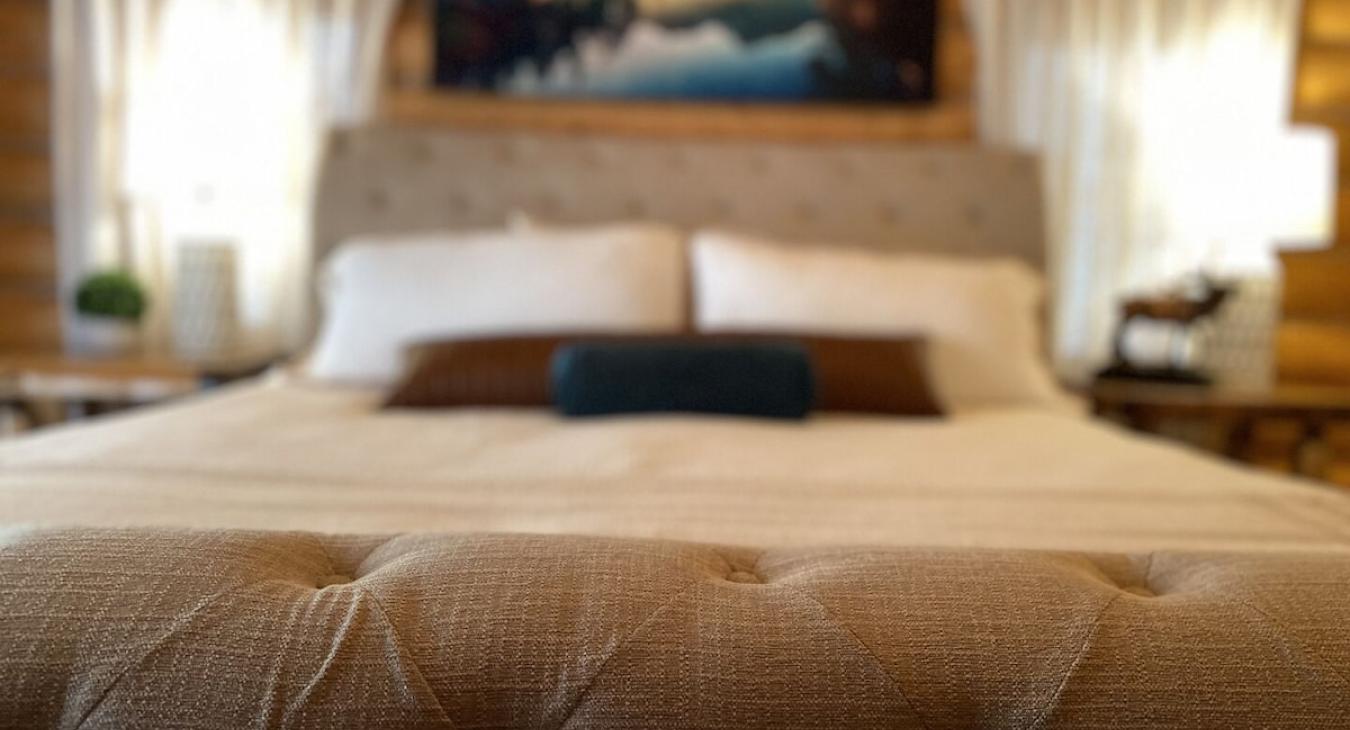 A large king-sized bed with a duvet is positioned at the center of the room, flanked by matching nightstands with stylish lamps that emit a soft, warm glow.