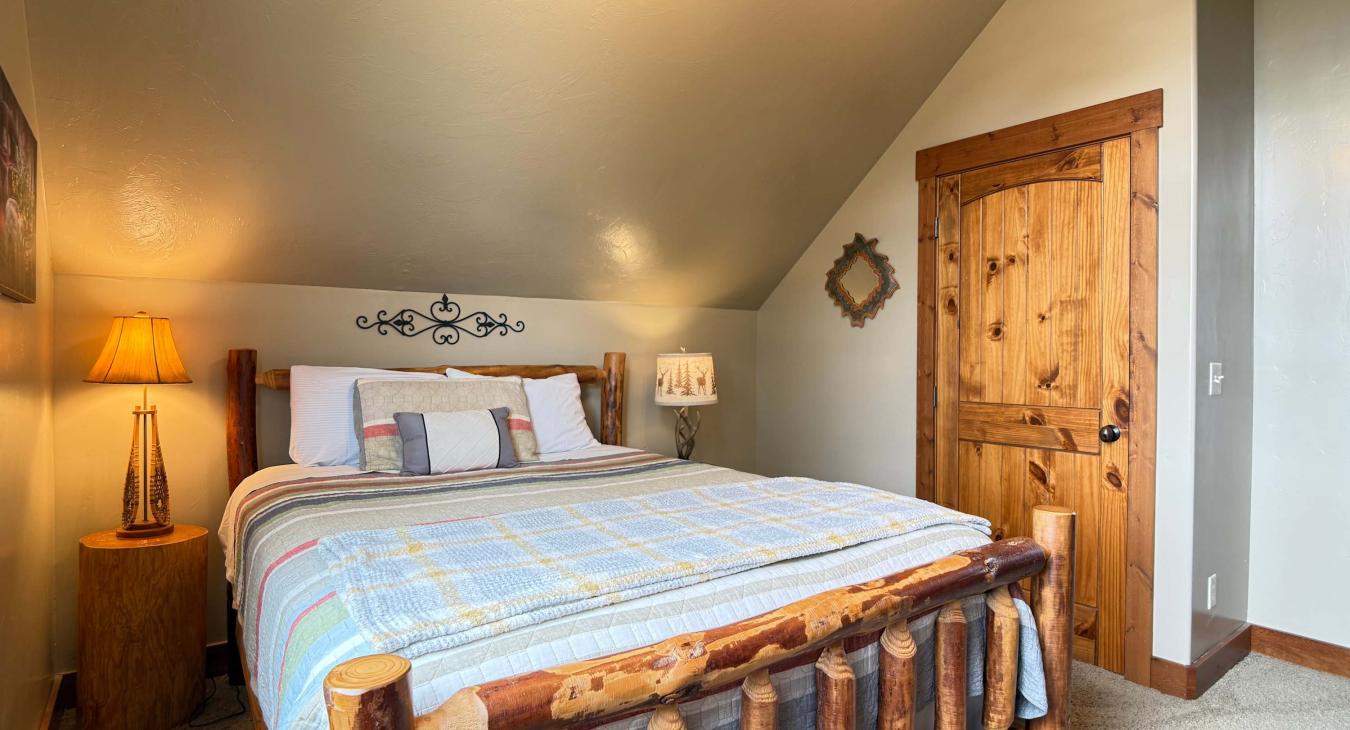 A charming upstairs bedroom nestled under the sloped cabin ceiling, complete with a cozy queen bed and rustic wooden accents.