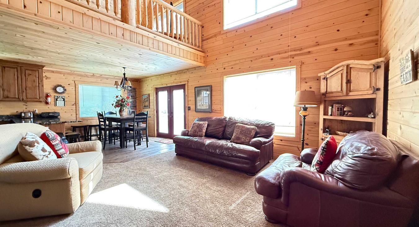 The grand, light-filled living room features soaring vaulted ceilings, a cozy open-loft design, and luxurious leather seating perfect for group conversations.