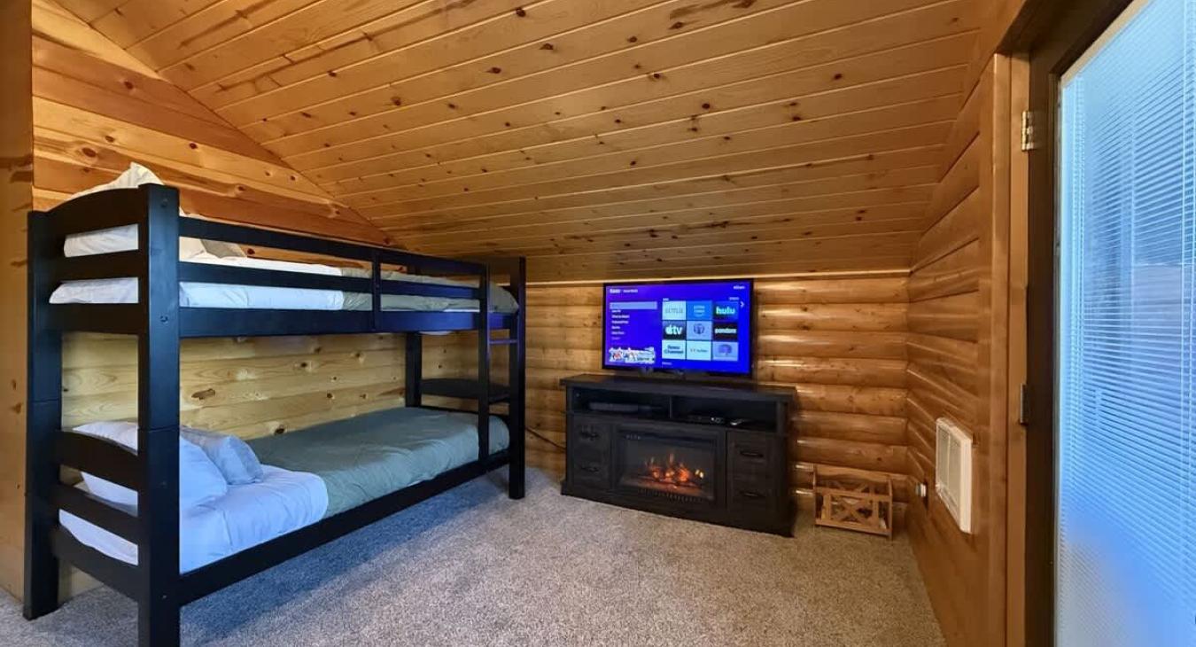 Upstairs loft with a single on single bunk bed with a smart tv and electric fireplace.