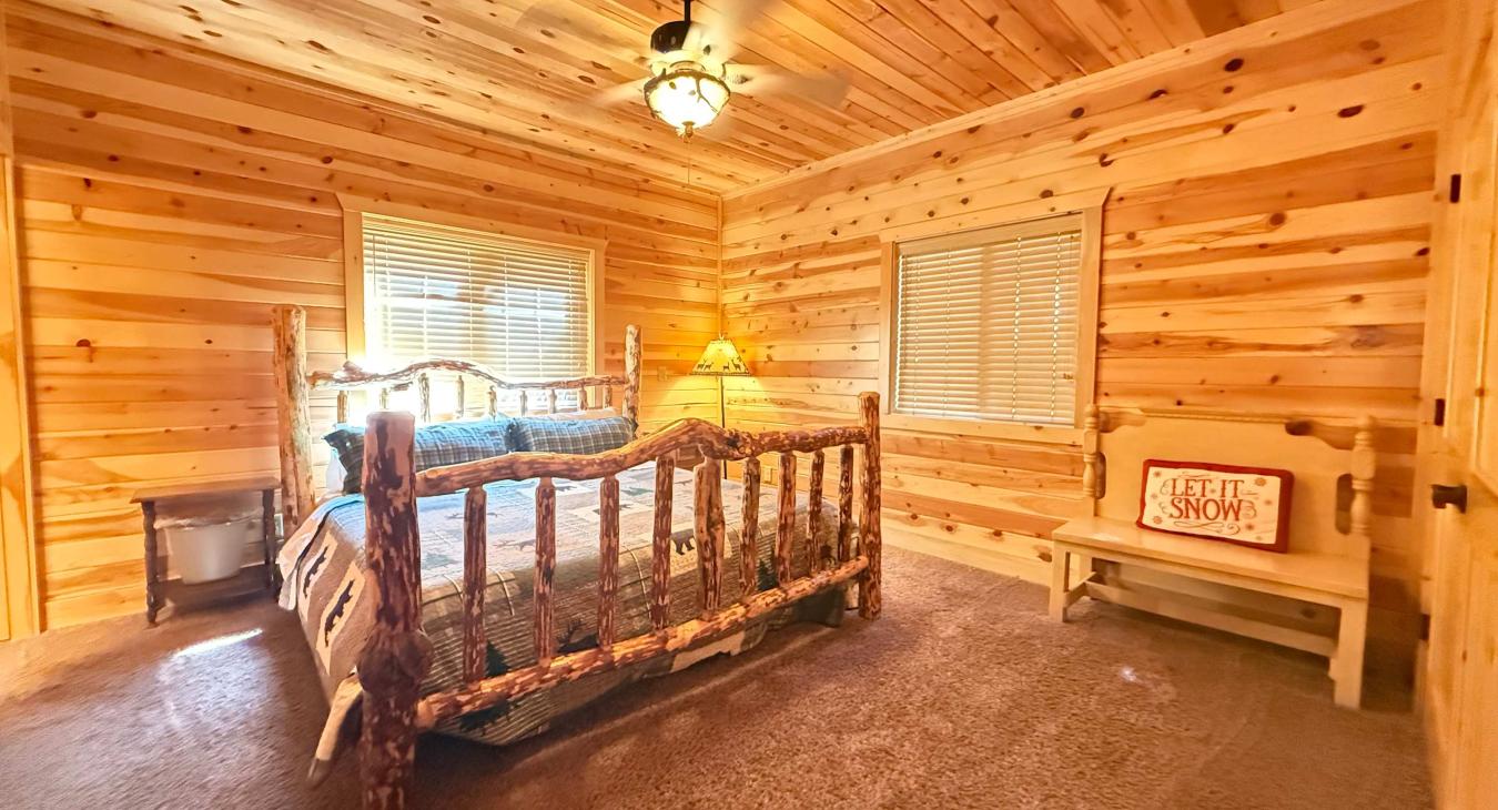 Unwind in the cozy master bedroom, showcasing a rustic log-framed King bed, beautiful all-wood paneled walls, and a charming wooden bench.