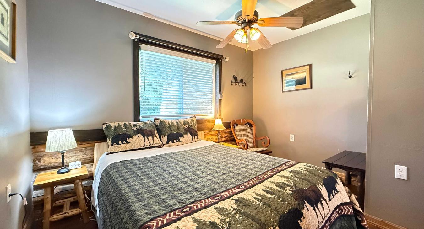 The second cozy bedroom features a comfortable log-framed Queen bed styled with a charming wilderness-themed quilt.