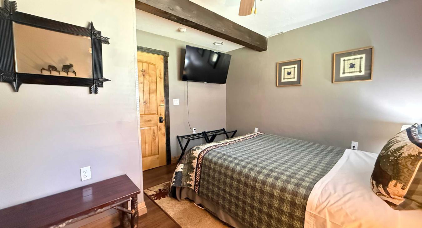 This warm guest room includes a wall-mounted flat-screen TV, rustic wall art, and a beautiful live-edge wooden bench at the entrance.