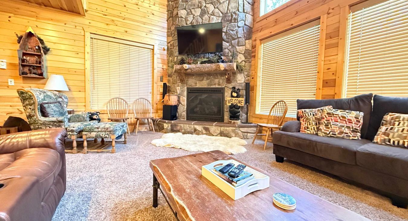 Relax in the grand living room, featuring a magnificent floor-to-ceiling stone fireplace, comfortable plush sofas, and a rustic live-edge coffee table.