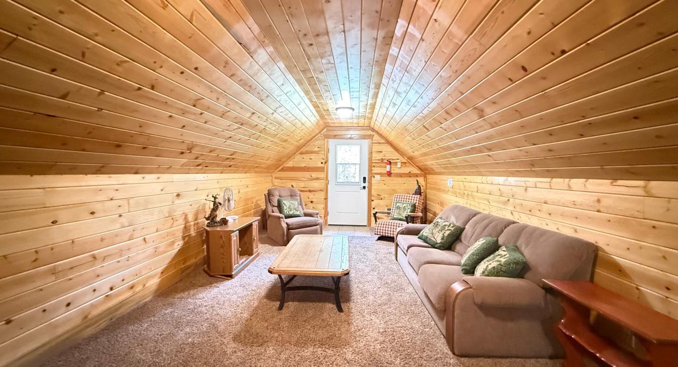 The spacious living area above the separate garage offers a cozy couch, armchairs, and a warm, rustic cabin atmosphere for extra privacy.