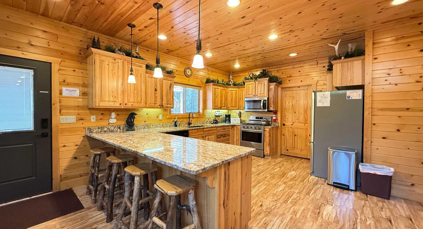 The fully equipped kitchen features gorgeous granite countertops and a spacious island with rustic log barstools, creating a perfect spot to gather.