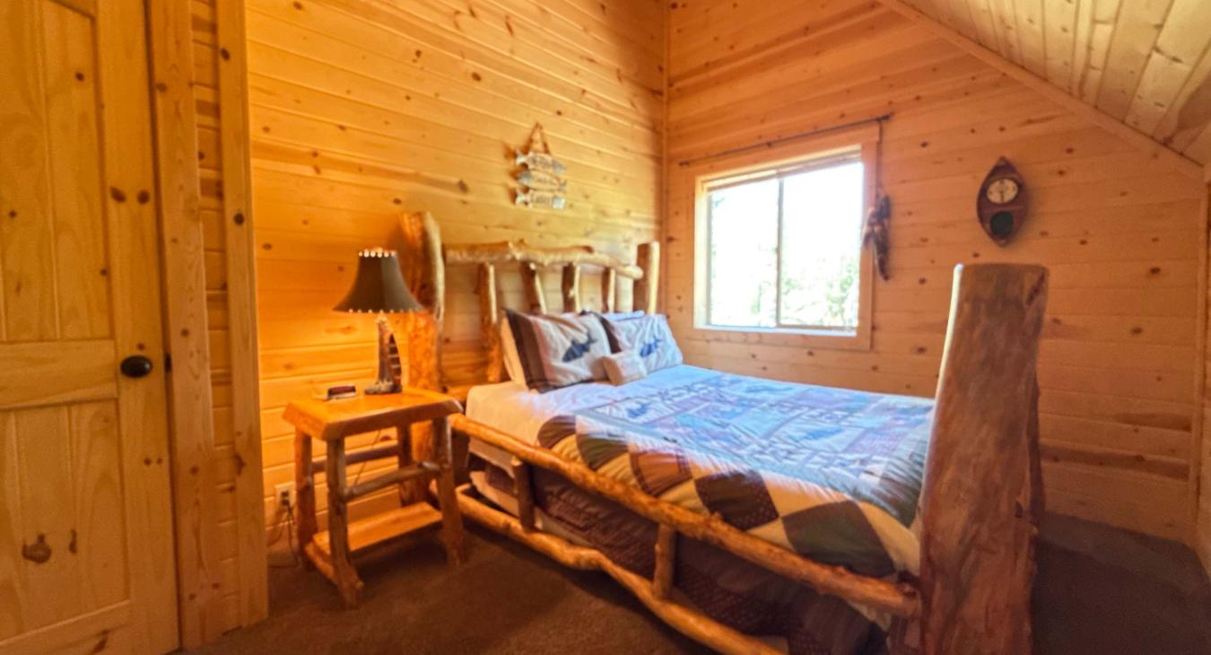 Bright and inviting, the third bedroom features a beautiful log-framed Queen bed styled with a charming wilderness-themed quilt.
