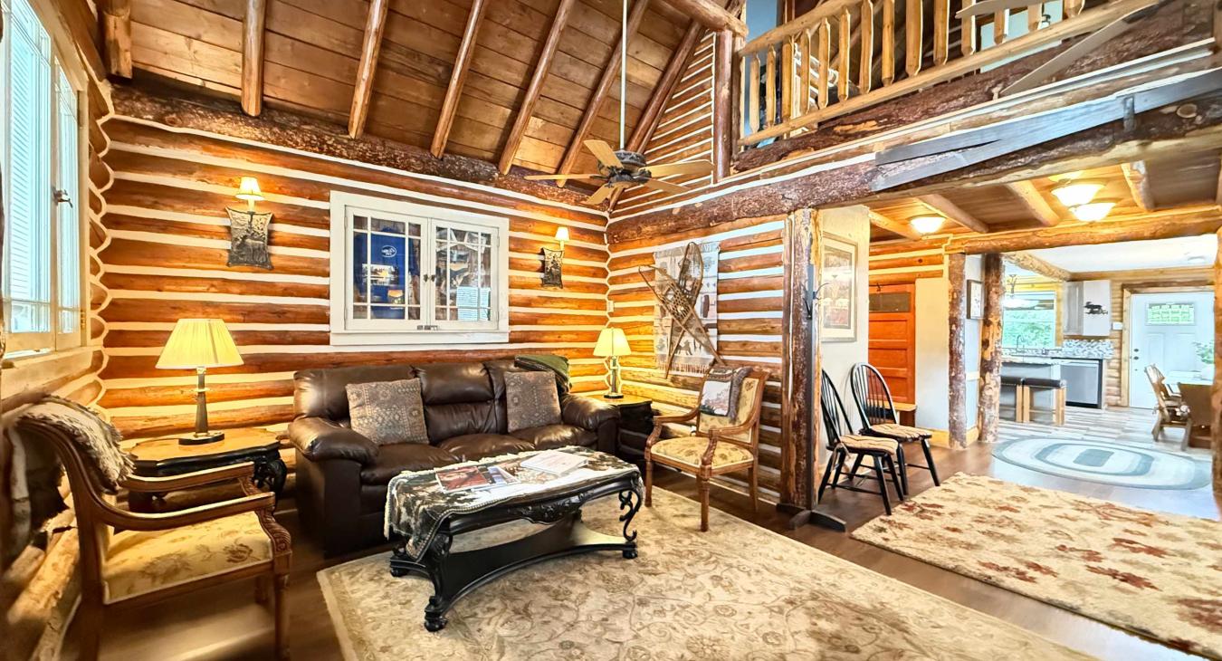 This breathtaking log cabin great room boasts soaring vaulted ceilings, rich wooden beams, and an open layout that leads into the dining space.