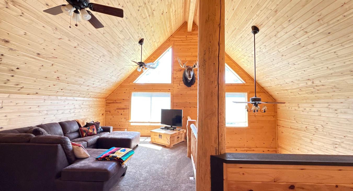 The cozy upstairs loft living room comes complete with a massive plush sectional sofa, a flat-screen TV, and authentic mountain-cabin decor.