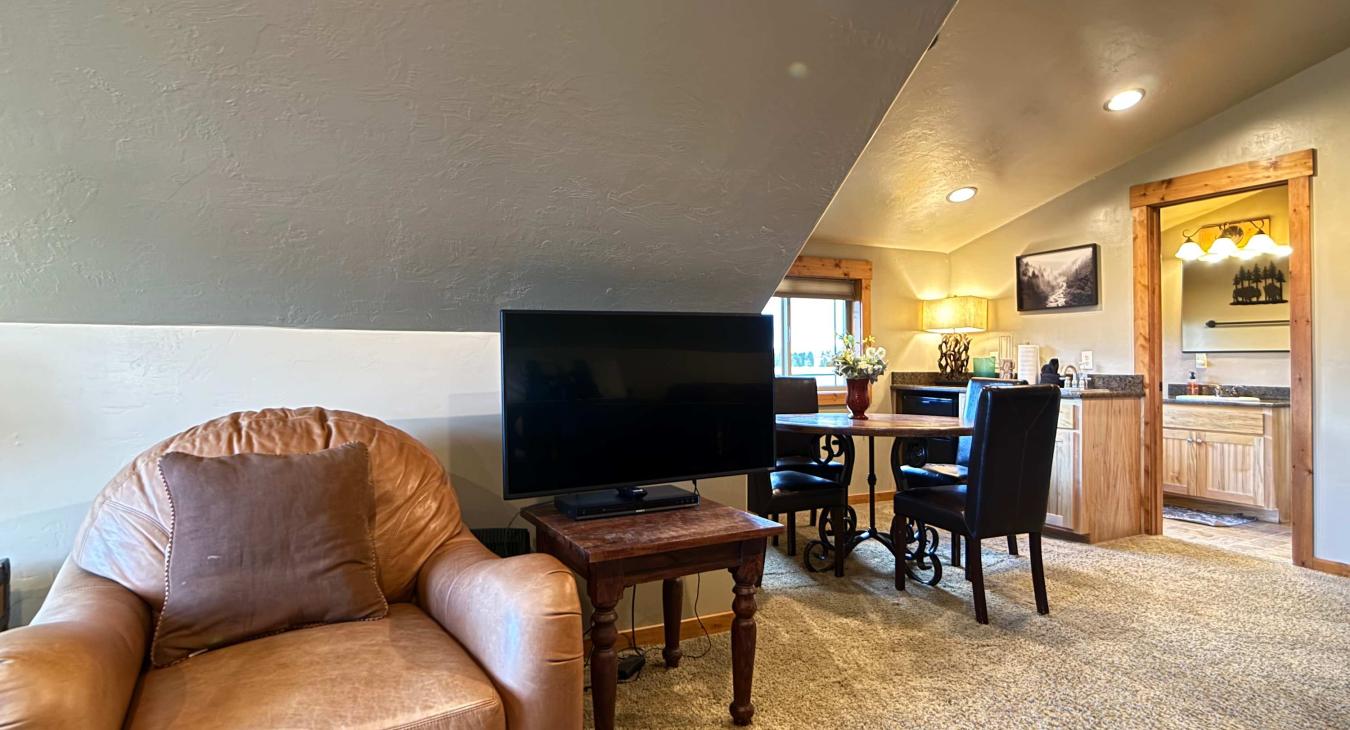 A wonderfully versatile guest suite nestled under sloped rustic ceilings, combining sleep, lounge, and dining options in one massive space.