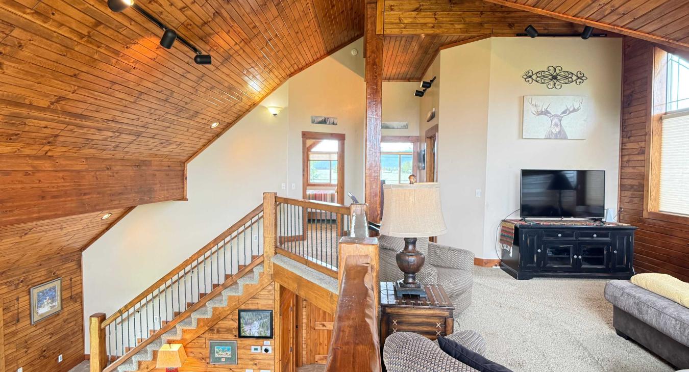 The grand loft area overlooks the main floor, showcasing the cabin's stunning vaulted architecture and rustic log railings.
