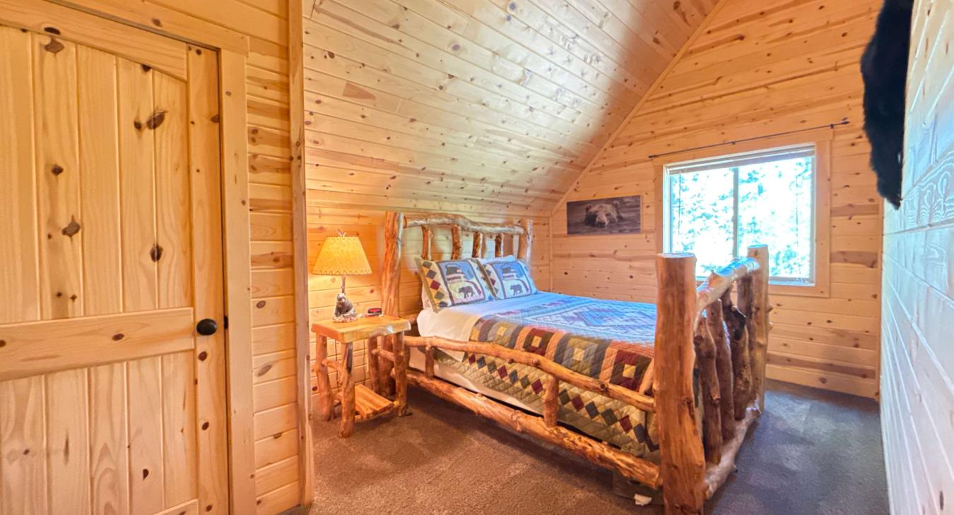 Escape to this cozy upstairs log retreat, featuring a masterfully crafted wood Queen bed beneath towering, dramatic A-frame ceilings.