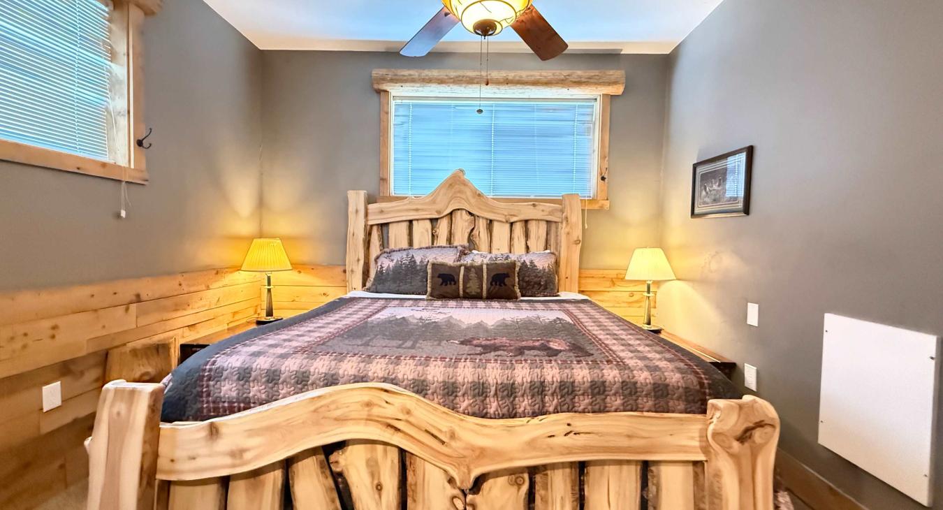 This peaceful bedroom features a beautifully crafted log-framed king bed, warm bedside lighting, and a rustic wilderness quilt.