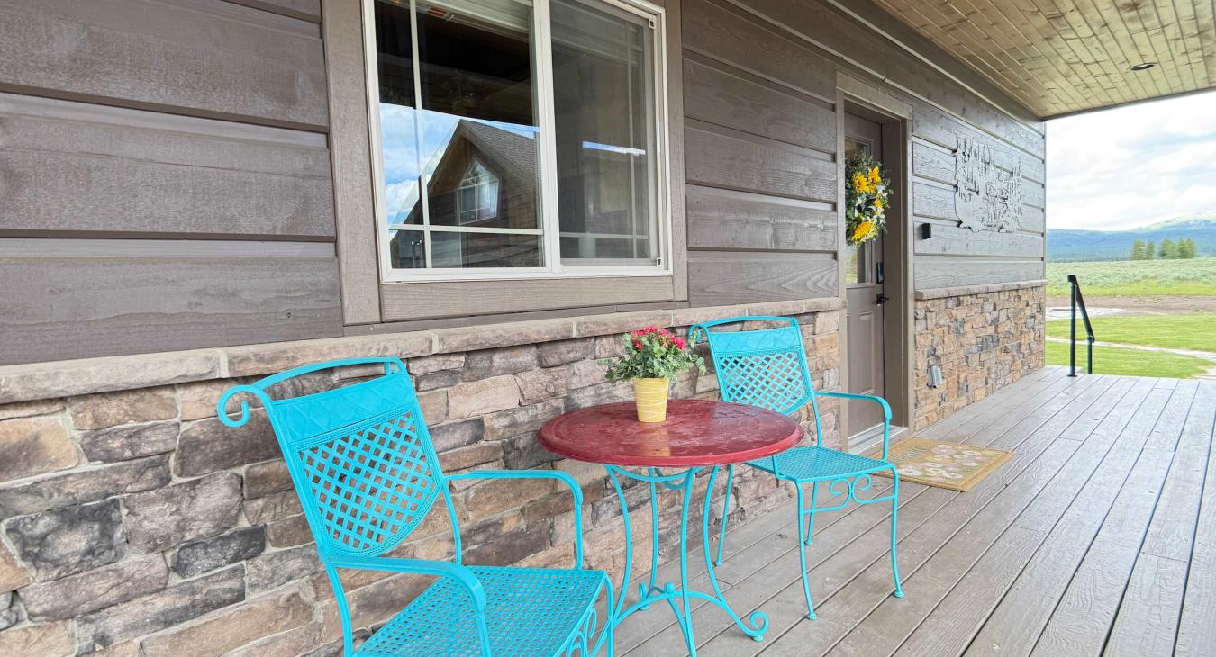 Relax on the charming front porch featuring bright turquoise seating and a small table—perfect for enjoying your morning coffee.