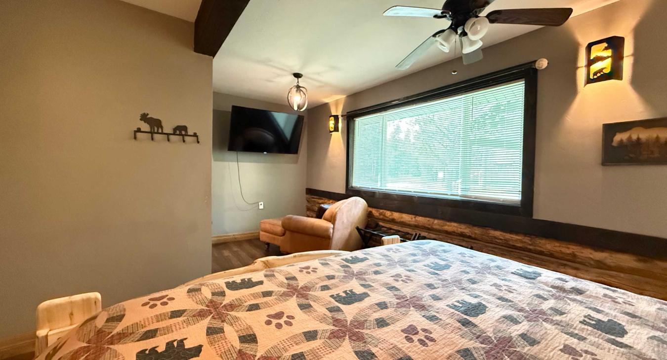 The spacious master suite also offers a private wall-mounted TV and a cozy leather armchair with an ottoman, perfect for a quiet reading escape.