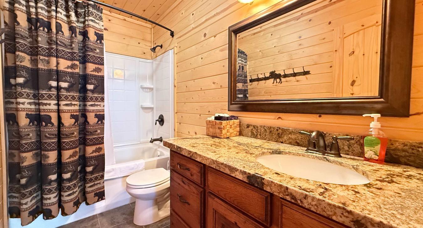 The convenience of an upstairs full bathroom—featuring a sparkling tub-and-shower combo, a premium granite-top vanity with ample storage, and a charming wilderness-themed curtain.