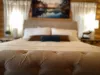 A large king-sized bed with a duvet is positioned at the center of the room, flanked by matching nightstands with stylish lamps that emit a soft, warm glow.