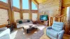 The room is well-lit by natural light pouring in from large, floor-to-ceiling windows. A flat-screen television is placed on the entertainment center, offering modern convenience without detracting from the cabin’s rustic appeal.