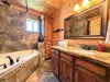 The luxury en-suite master bathroom boasts a large custom wooden vanity with a premium granite countertop, bright lighting, and a deep soaking jetted tub.